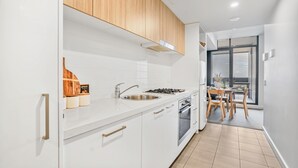 Eine moderne Küche mit weißen Schränken, einer Spüle aus Edelstahl, Holzschränken über dem Herd und einem Essbereich mit Tisch und Stühlen.