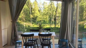 Quarto com vista para uma floresta, mesa de jantar com cadeiras e sofá com almofadas.