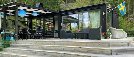 A modern outdoor deck with outdoor seating, a flag, and a view of a forested area.