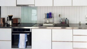 Uma cozinha moderna com armários brancos, bancada de aço inoxidável, máquina de café, torradeira e escorredor de louça.