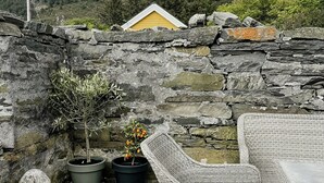 Un muro de piedra, un edificio amarillo, una planta en maceta y muebles de mimbre.