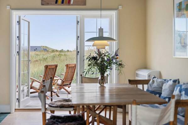 An open sliding door leading to a patio with outdoor seating and a view of a grassy field. - Historic house near Råbjerg Mile and North Sea (Skagen)