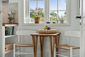 A kitchen with white cabinetry, a window with a view, a table with a woven basket, and two white chairs. - Historic house near Råbjerg Mile and North Sea (Skagen)