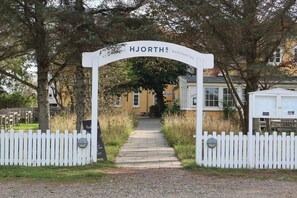A white archway with 'HJORTH'S BAEHOTEL' written on it, leading to a pathway flanked by white picket fences. - Historic house near Råbjerg Mile and North Sea (Skagen)