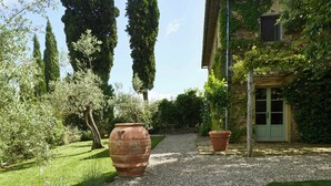 Un jardin avec un chemin de gravier, de grands arbres et de grands pots en terre cuite.