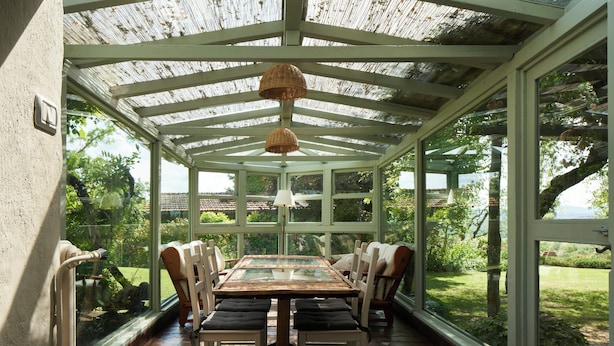 Une véranda avec une table et des chaises en verre, entourée de grandes fenêtres.