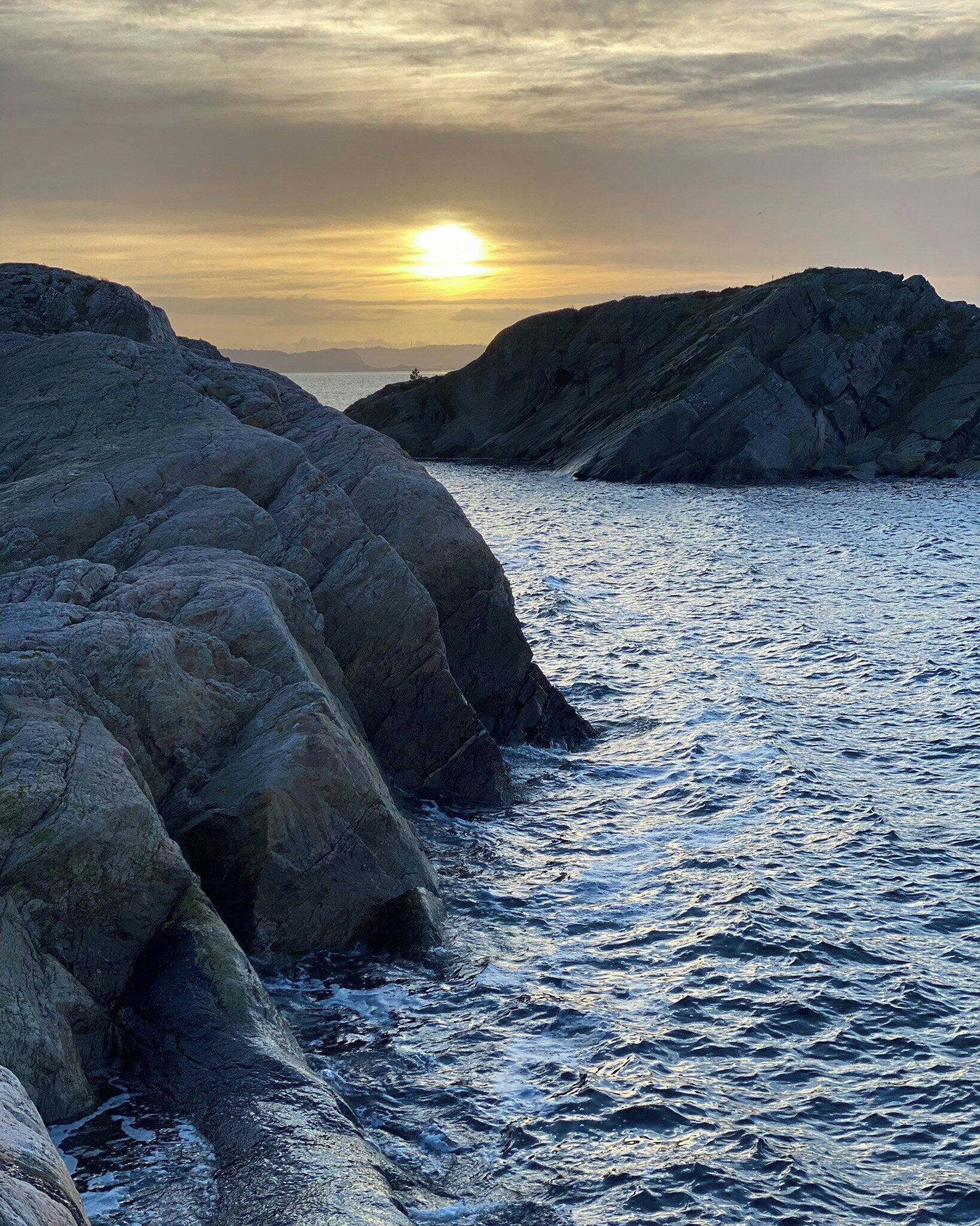 A rocky coastline with the sun setting over the water.