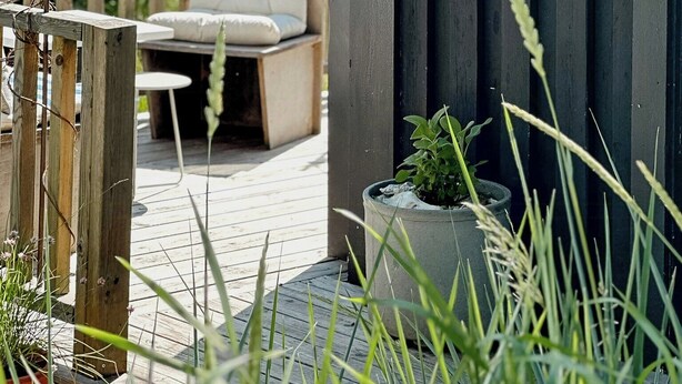 Een houten terras met een zithoek, een bloempot en een wandlamp.