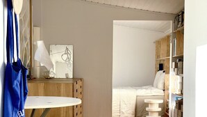 Een compacte kamer met een houten vloer, een klein rond tafeltje met krukjes, een bed en een boekenkast.