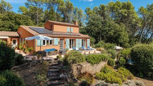 Een huis in mediterrane stijl met een stenen trap, terras en uitzicht op het omliggende bos.