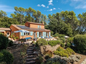 Ein mediterranes Haus mit einer Steinstufe, Sitzgelegenheiten im Freien und Blick auf den umliegenden Wald.