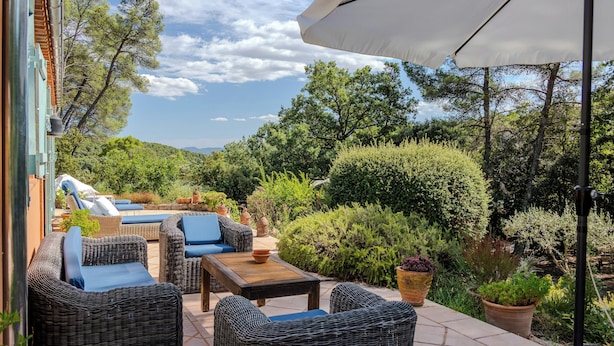 Een terras buiten met rieten meubels, een tafel en een grote parasol.
