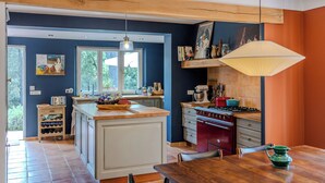 Een keuken met een centraal eiland, een rode kookplaat en een hangende lamp.