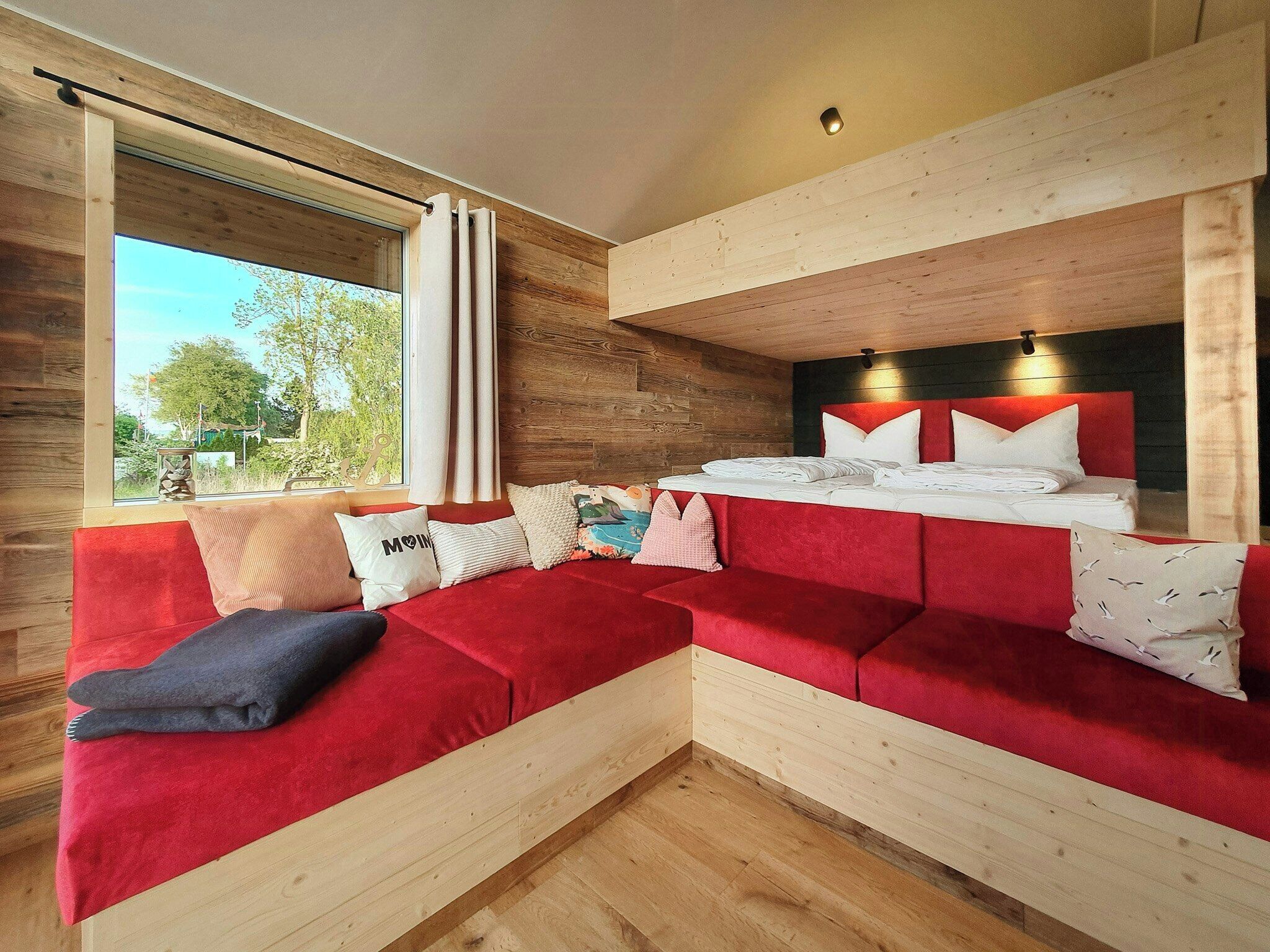 A modern room with a wooden floor, a red sofa, a bed with white bedding, and a window with curtains.