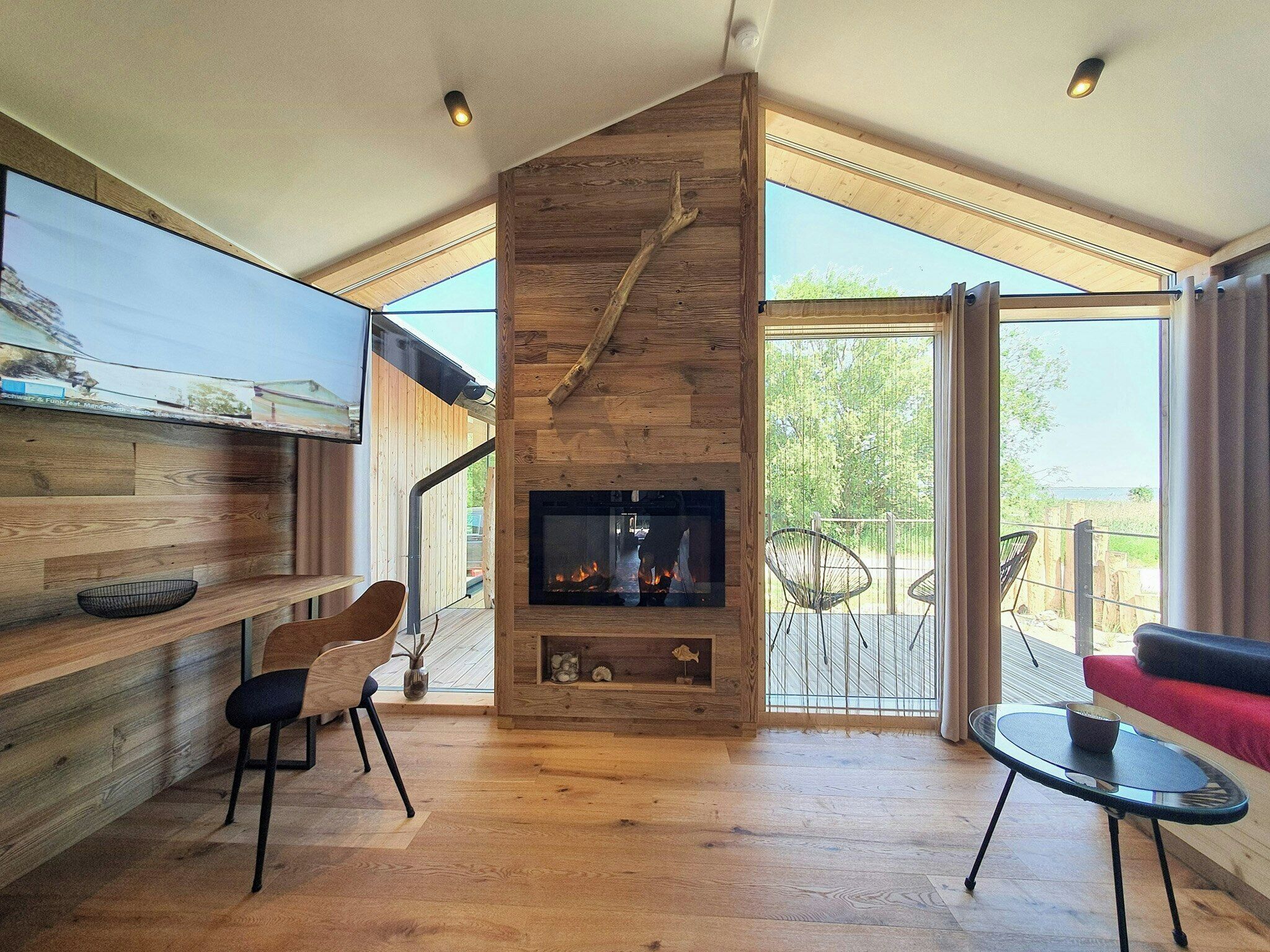 A modern interior with a fireplace, wooden walls, and a balcony with outdoor seating.