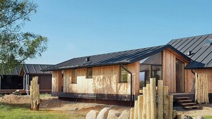 A wooden cabin with a sloped roof, large windows, and a stone foundation. - Tiny chalet with sea view at Werder (Boiensdorf)