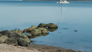 A calm body of water with a sailboat anchored in the distance, surrounded by rocks and a sandy beach. - Tiny chalet with sea view at Werder (Boiensdorf)
