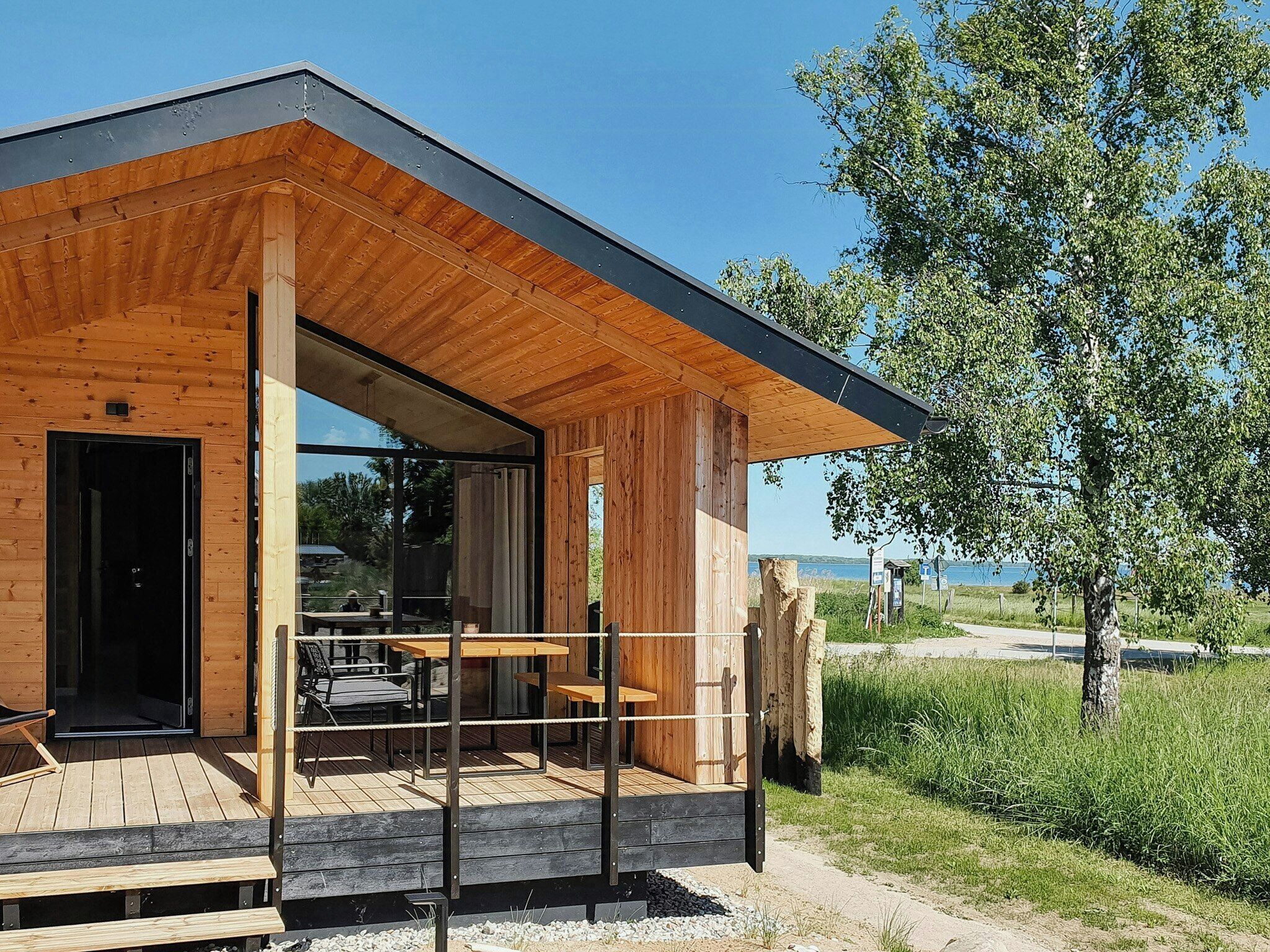 Una cabaña moderna de madera con terraza, ventanas grandes y vistas al paisaje.