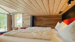 A bedroom with a wooden ceiling, a large bed with white bedding, a window with curtains, and a view of greenery outside. - Tiny chalet with sea view at Werder (Boiensdorf)