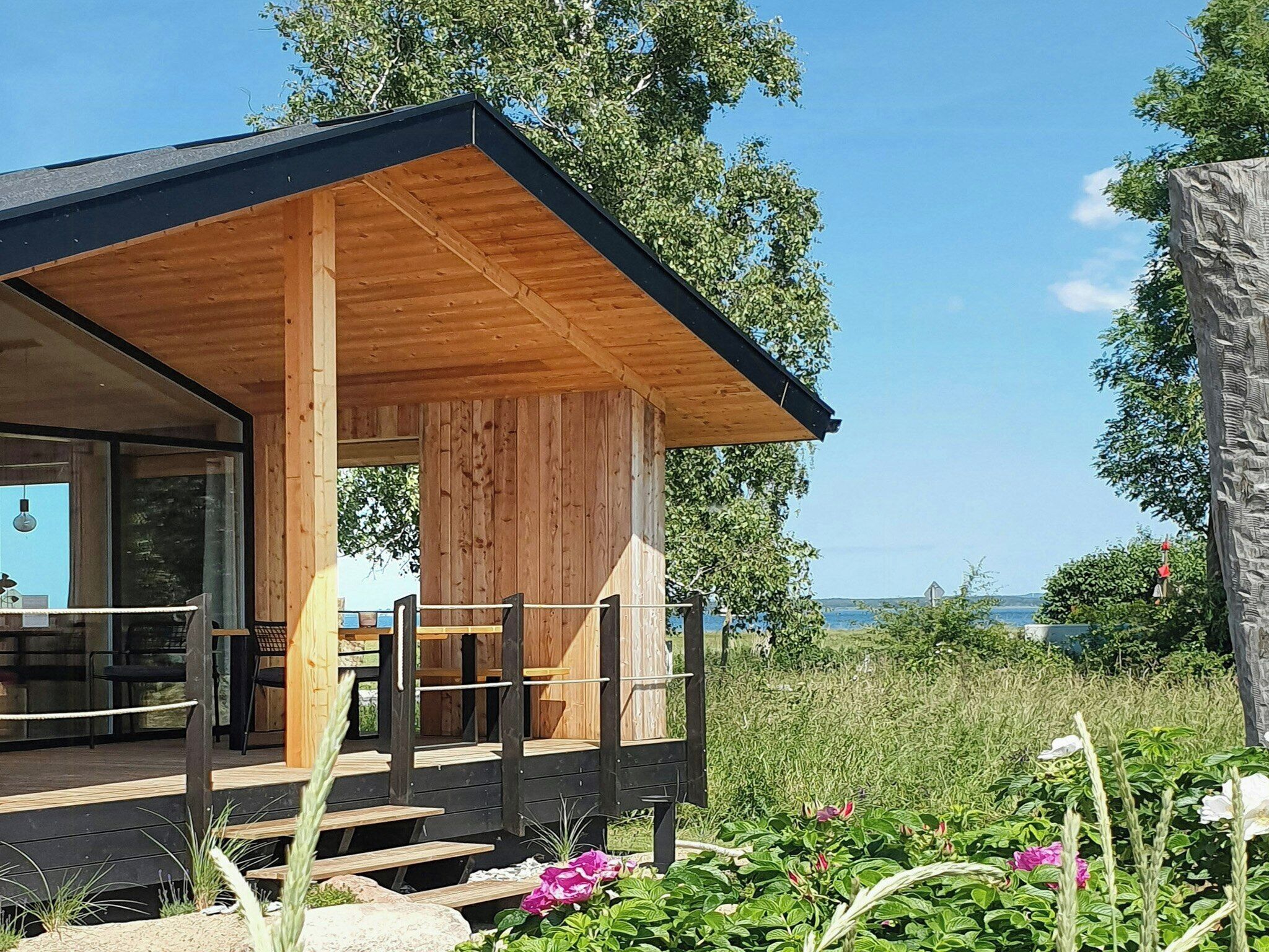 A modern wooden cabin with a covered porch, outdoor seating, and a view of the landscape.