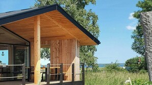 A modern wooden cabin with a covered porch, outdoor seating, and a view of the landscape. - Tiny chalet with sea view at Werder (Boiensdorf)