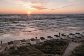 Una playa con cabañas blancas y el sol poniéndose sobre el océano.