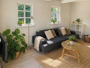 Una sala de estar acogedora con un sofá gris oscuro, una mesa de centro redonda de mimbre y una planta grande.