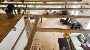 Een meerlaags houten interieur met een trap, een eetgedeelte en een zithoek met een bank en kussens.