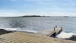 Een houten steiger die zich uitstrekt over kalm water, met een land in de verte en een heldere lucht.