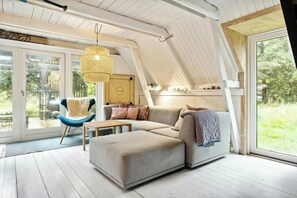 A cozy living room with a sectional sofa, a blue chair, and a hanging light fixture. - Cosy little wooden house on natural grounds (Vestervig)