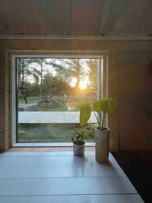 A window with a view of a wooden deck and a sunset. - Cosy little wooden house on natural grounds (Vestervig)