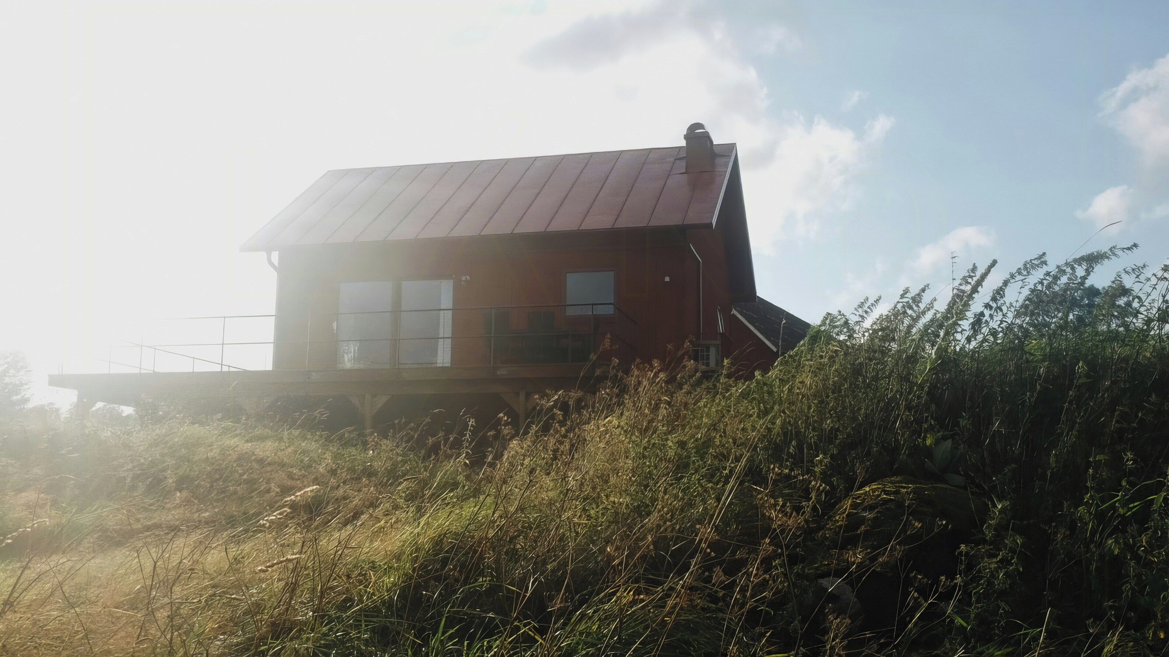 Un bâtiment d’un seul étage, doté d’un toit en pente, entouré d’herbes hautes et de végétation.