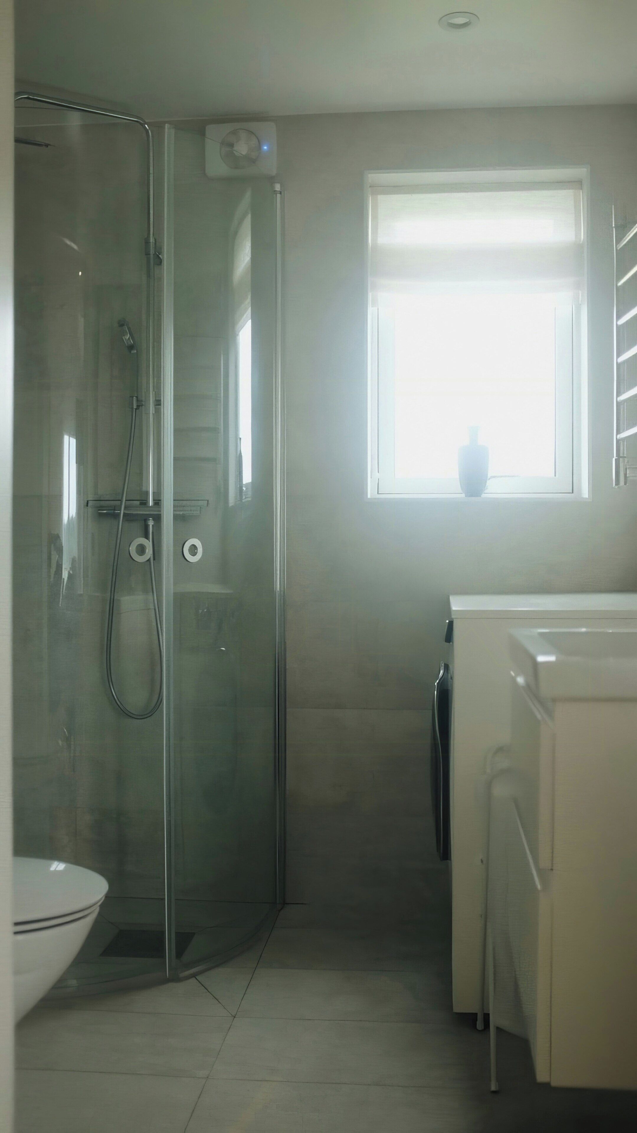 A bathroom with a glass shower enclosure, a toilet, and a window with blinds.