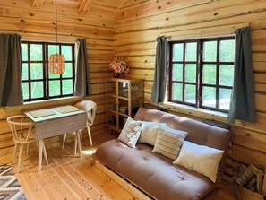 Ein Holzblockbau-Innenraum mit einer Couch, einem Tisch und zwei mit Vorhängen versehenen Fenstern.