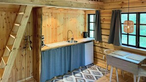 Interior de una cabaña de madera con habitación en loft, una cocina con lavabo y cafetera, y un comedor con mesa y sillas.