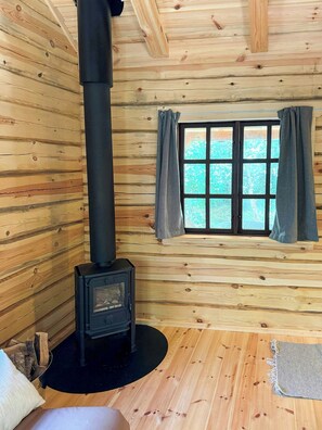 Ein Blockhaus-Interieur mit Kaminofen, einem Fenster mit Vorhängen und einer gemütlichen Sitzecke.