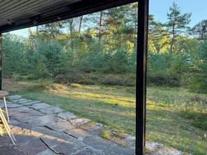 Ein überdachter Außenbereich mit Steinböden, einer Holzbank und Blick auf eine bewaldete Landschaft.