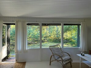 Ein Zimmer mit einem großen Fenster, einem Korbstuhl und einem weißen Tisch.