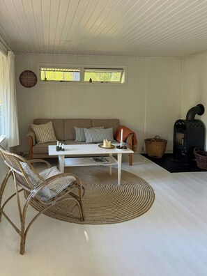 Ein Wohnzimmer mit einer Couch, einem Couchtisch, Korbstühlen, einem Kamin und einem Fenster mit Vorhängen.