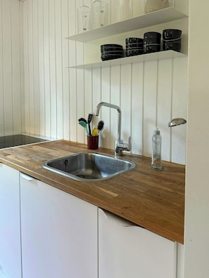 A kitchen with a stainless steel sink, wooden countertop, and white cabinetry. - Holiday home by forest and beach on Bornholm (Aakirkeby)