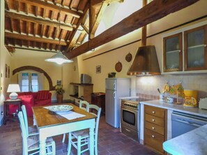 A kitchen with a dining table, chairs, a stove, a refrigerator, and a hanging pot rack. - Quiet Getaway in the Heart of Tuscany (Segromigno in Monte)