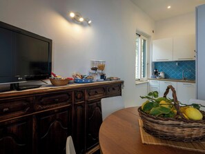 A modern kitchen with a flat-screen TV, wooden cabinets, a dining table, and a basket of lemons. - Sea view house with lemon grove in Atrani (Ravello)