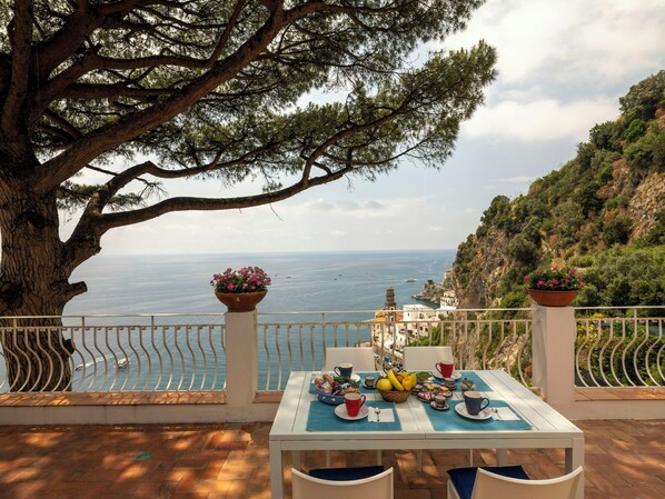 A table set outdoors with a view of the sea and a mountainous backdrop. - Sea view house with lemon grove in Atrani (Ravello)