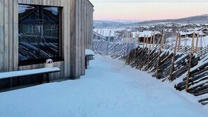 Un edificio de madera con un gran ventanal, un sendero cubierto de nieve y vistas a un paisaje nevado.