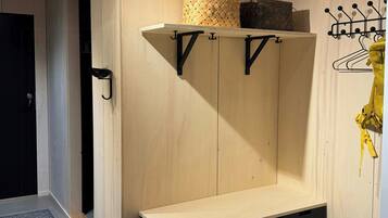 A room with a wooden wardrobe, a bench with storage drawers, a hanging coat rack, and a patterned rug.