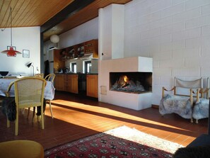 Ein Wohnzimmer mit Kamin, Holzmöbeln und einer Küche im Hintergrund.