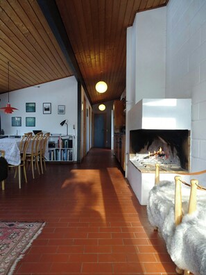 Ein langer Korridor mit Kamin, Holzboden und einem Essbereich mit Stühlen und Tisch.