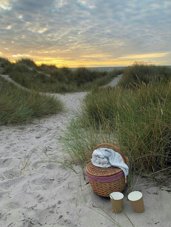 Ein Strandweg mit Sand, Gras und einem Korbwiegungskorb mit Stoff und zwei Papierbechern.