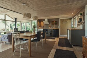 Eine moderne Küche mit Holzschränken, ein Essbereich mit Tisch und Stühlen und ein großes Fenster, das für natürliches Licht sorgt.