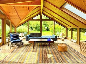 Une pièce spacieuse avec un plafond haut, un canapé, un fauteuil, une table basse et un tapis à motifs.